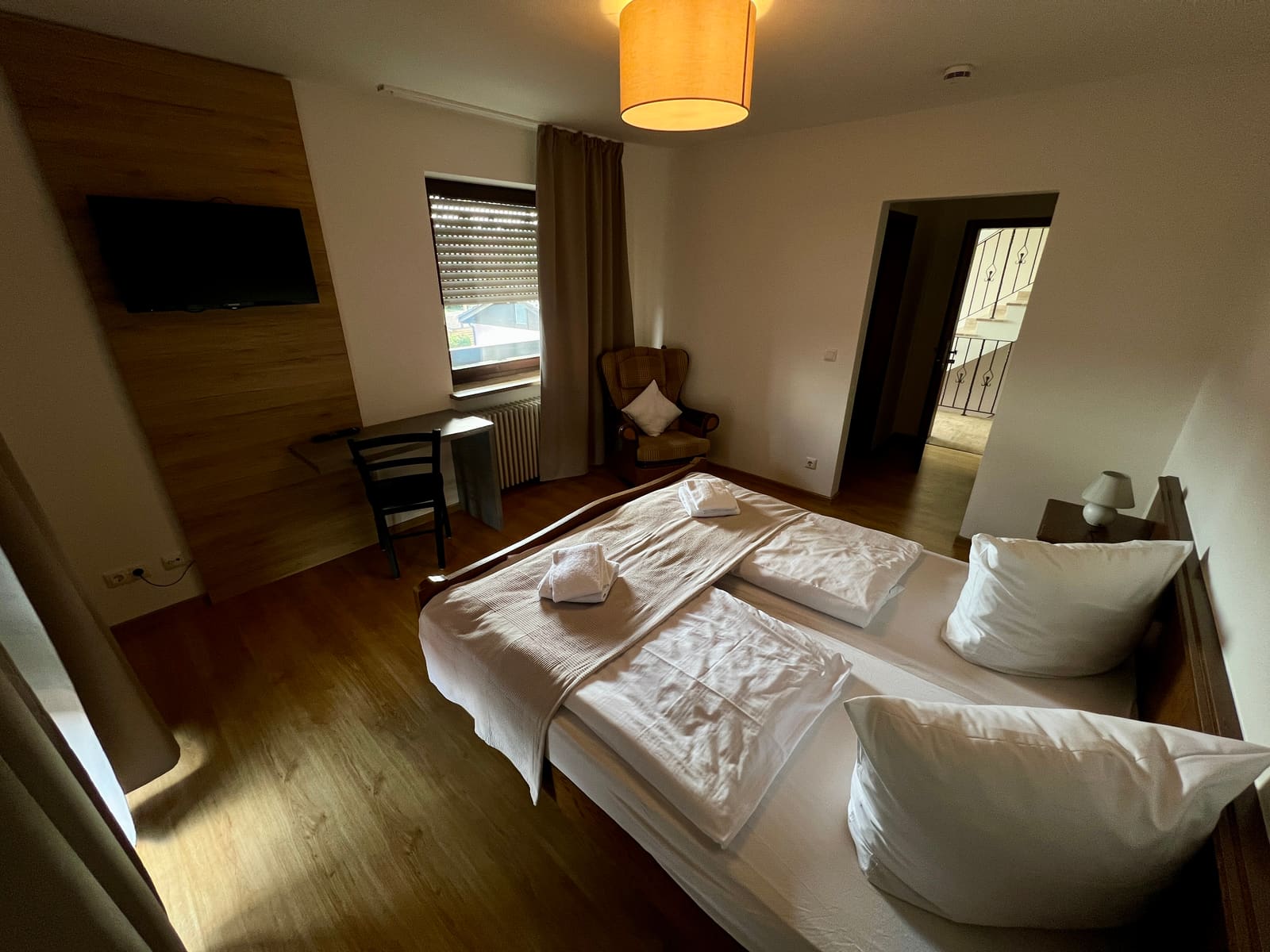 Gästezimmer 1 im Gasthof Dorfwirt Fridolfing – Doppelbett, Holzwand und Sessel am Fenster