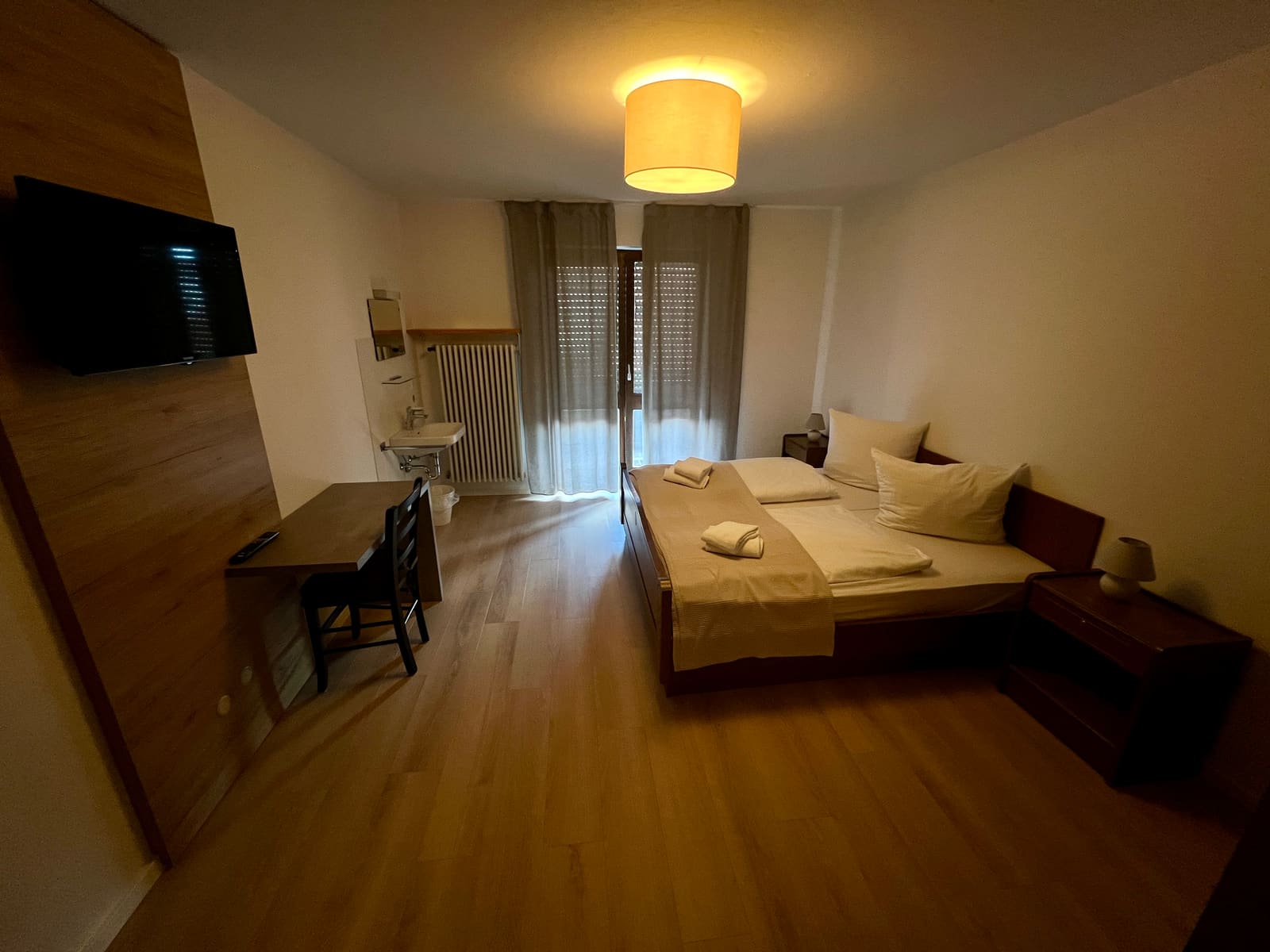 Zimmer 2: Doppelbett, Schreibtisch und Fernseher, im Hintergrund Fenster und Waschbecken
