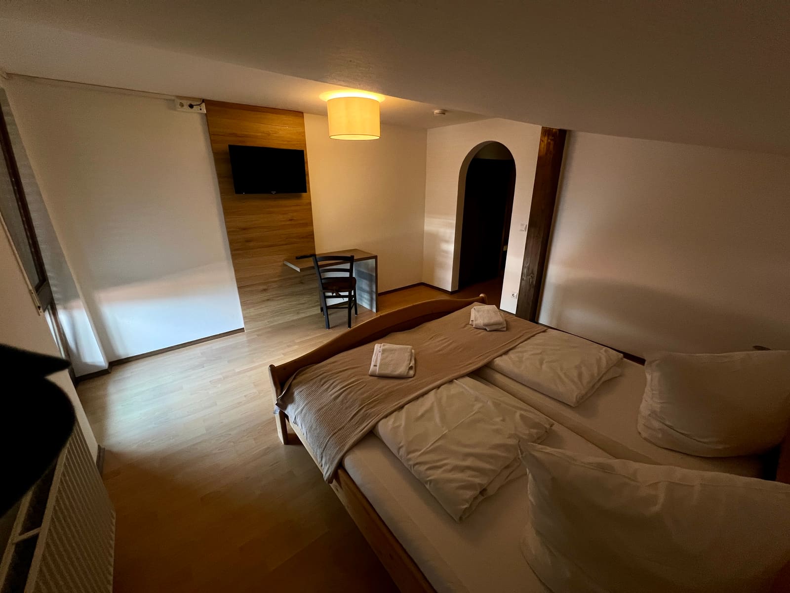 Zimmer 5: Doppelbett, Schreibtisch vor der Holzwand und Rundbogentür